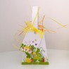 Panier  de Pâques en papier avec son étiquette assortie décorée de motifs colorés et d'un petit lapin dans l'herbe.
